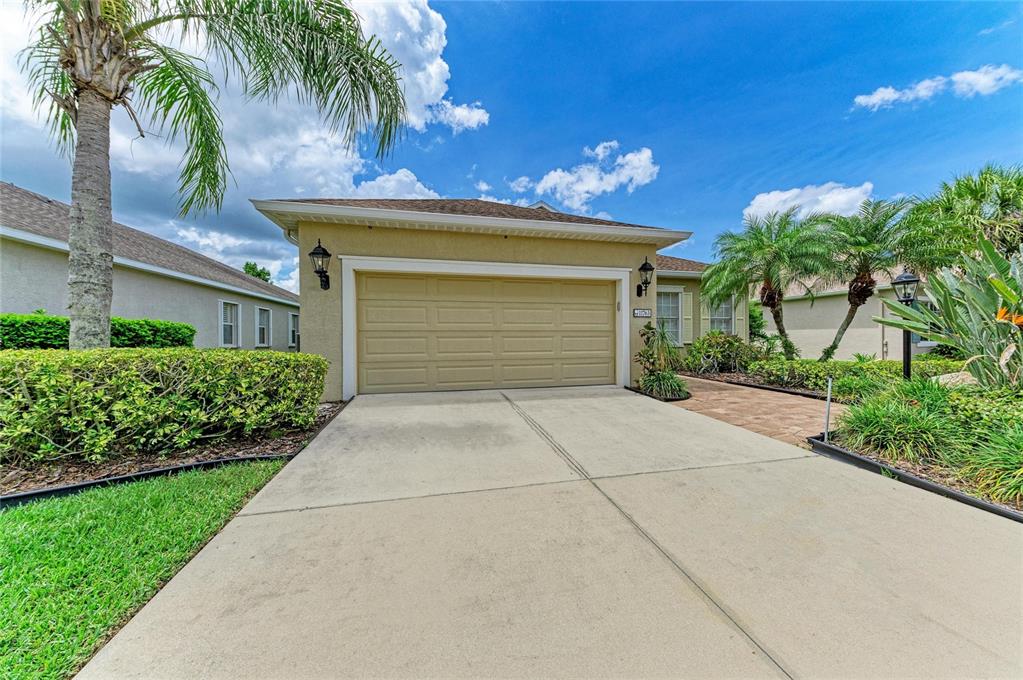 A beige house exterior features a two-car garage, a concrete driveway, and surrounding palm trees — 11763 FENNEMORE WAY, PARRISH, FL