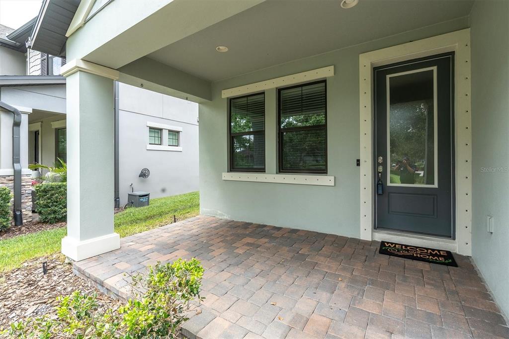 A covered front porch features paver flooring, a dark door, and two windows — 3343 HEART PINE AVENUE, ODESSA, FL