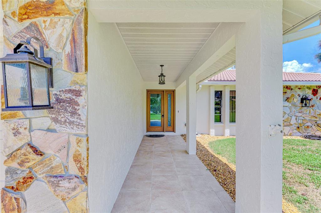 A covered entryway features stone-clad walls, a tiled floor, and a wooden front door — 2340 PALMETTO STREET, NOKOMIS, FL