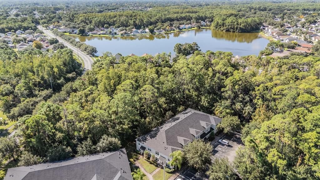 An aerial view shows a multi-story apartment building surrounded by dense trees near a lake — 9624 CHARLESBERG DRIVE, TAMPA, FL