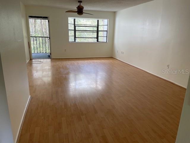 An empty living room features light wood-look flooring, a ceiling fan, and a sliding glass door — 11550 BAYWOOD MEADOWS DRIVE UNIT 7, NEW PORT RICHEY, FL