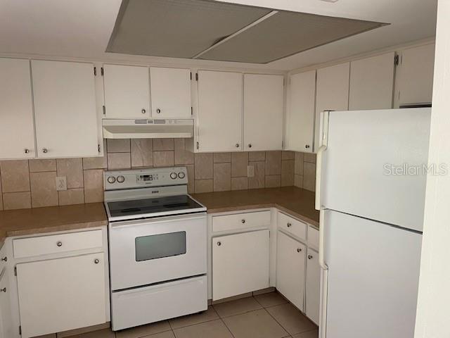 A kitchen features white cabinets, a white stove, a white refrigerator, and tiled backsplash — 11550 BAYWOOD MEADOWS DRIVE UNIT 7, NEW PORT RICHEY, FL