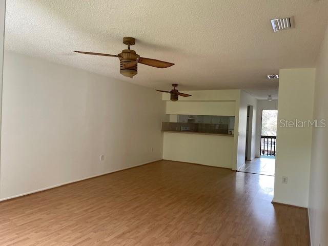 An open-concept living area features light wood-look flooring, two ceiling fans, and a kitchen pass-through — 11550 BAYWOOD MEADOWS DRIVE UNIT 7, NEW PORT RICHEY, FL