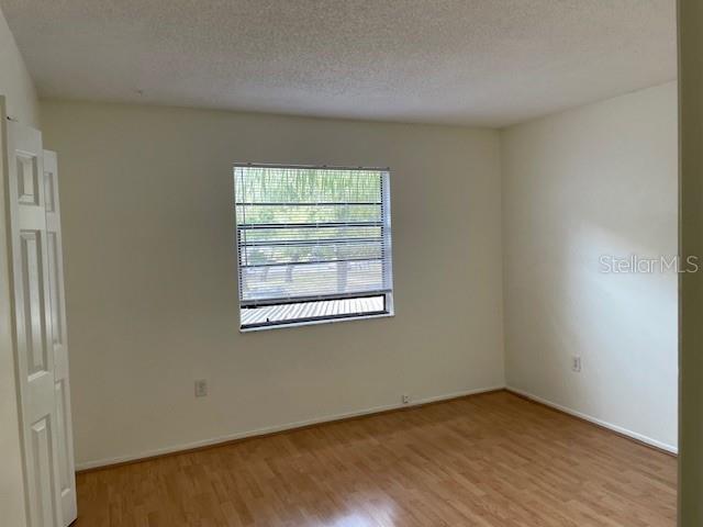 An empty bedroom features light-colored walls, wood-look flooring, and a single window with blinds — 11550 BAYWOOD MEADOWS DRIVE UNIT 7, NEW PORT RICHEY, FL