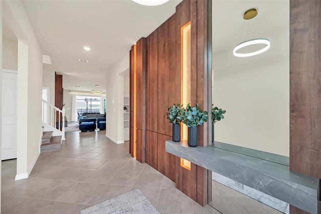 A modern entryway features a wood-paneled accent wall with integrated lighting, a floating stone console, and tile flooring — 16248 SAINT MARTIN STREET, CLERMONT, FL