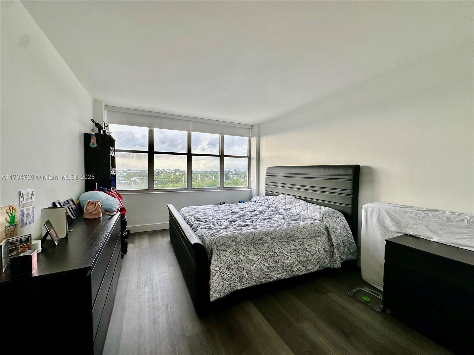 A bedroom features a dark bed frame, a long dresser, and large windows with city views — 7441 Wayne Ave # 6B, Miami Beach FL 33141, MIAMI BEACH, FL