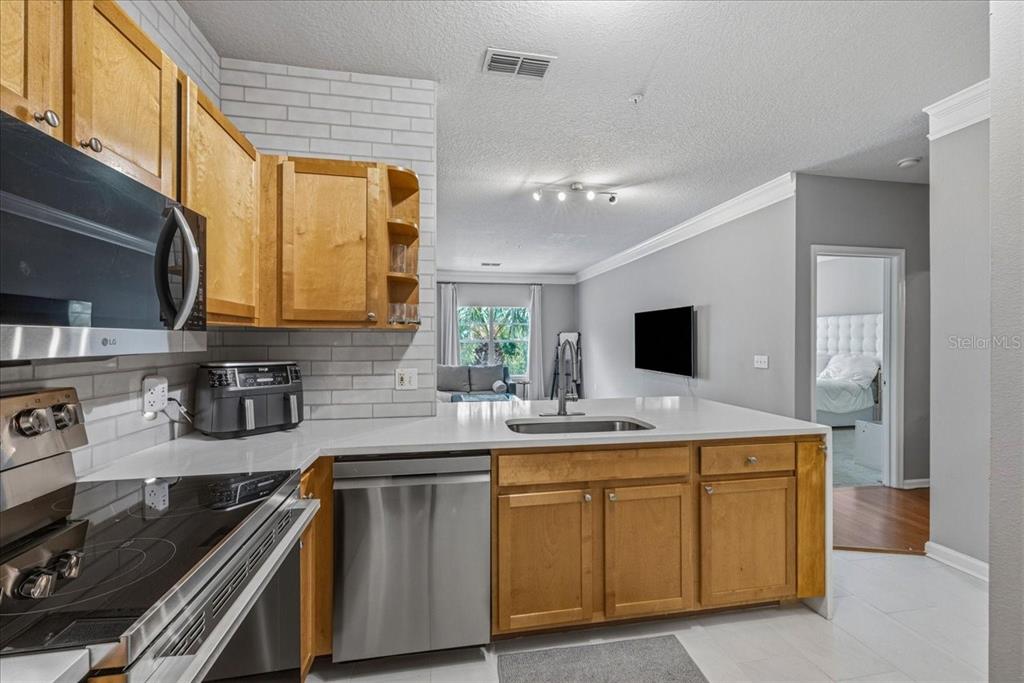 A kitchen with light wood cabinets, stainless steel appliances, and white countertops overlooks a living area — 4207 S DALE MABRY HIGHWAY UNIT 8308, TAMPA, FL