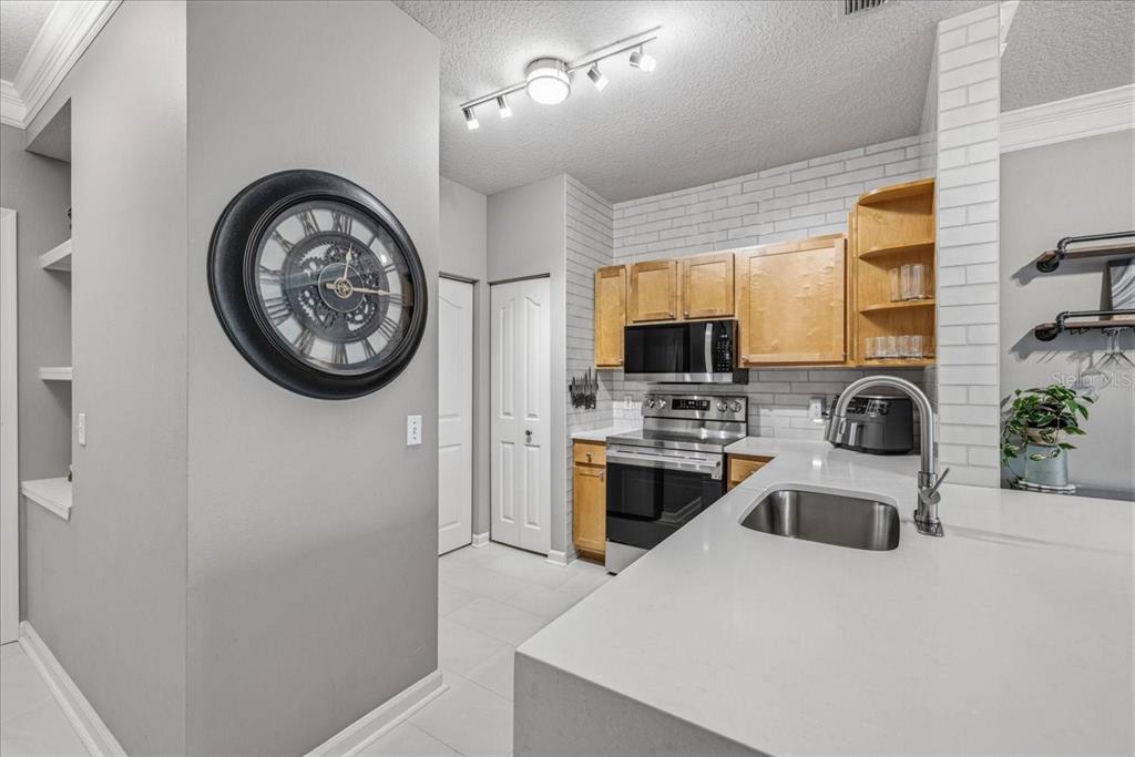 A kitchen features light wood cabinets, white subway tile backsplash, quartz countertops, and a wall clock — 4207 S DALE MABRY HIGHWAY UNIT 8308, TAMPA, FL