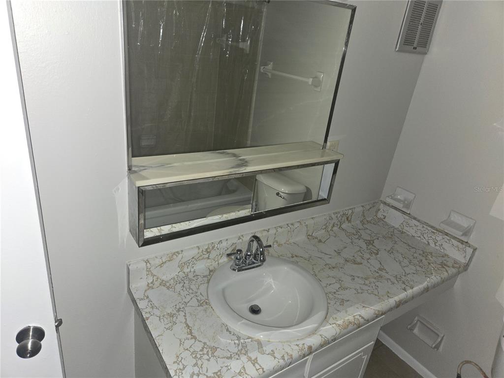 A bathroom vanity features a white sink, marble-patterned countertop, and a large wall-mounted mirror — 1935 CONWAY ROAD UNIT O5, ORLANDO, FL