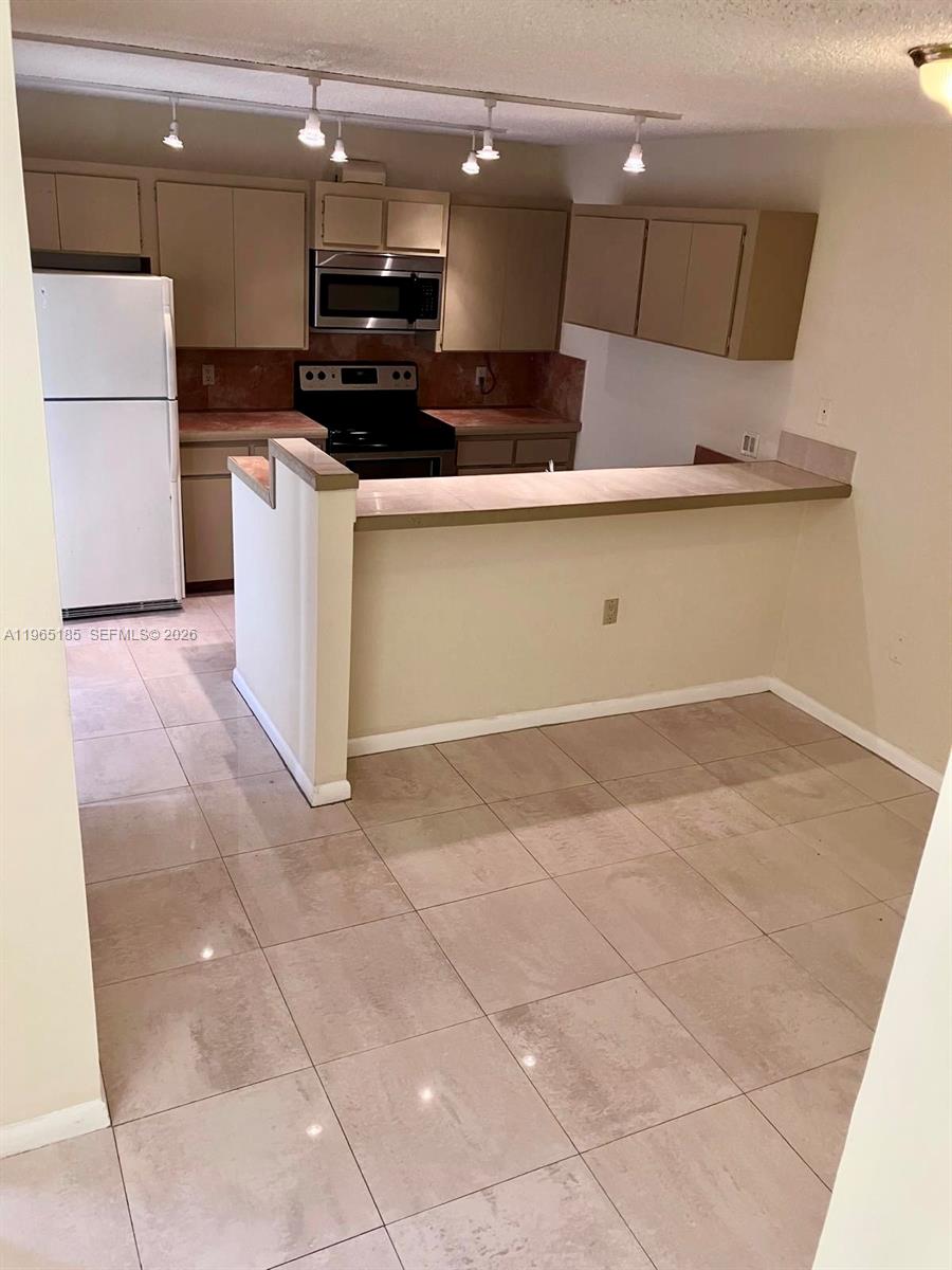 A kitchen features beige cabinets, a white refrigerator, and a breakfast bar with tile flooring — 2610 26th way, Riviera Beach FL 33407, RIVIERA BEACH, FL