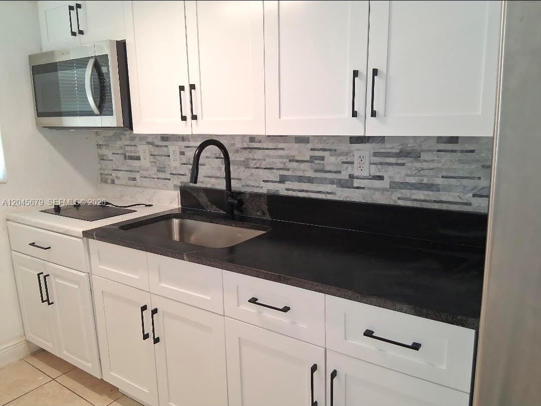 A kitchen features white cabinets, a black countertop, a stainless steel sink, and tiled backsplash — 3901 SW 112th Ave # 24, Miami FL 33165, MIAMI, FL