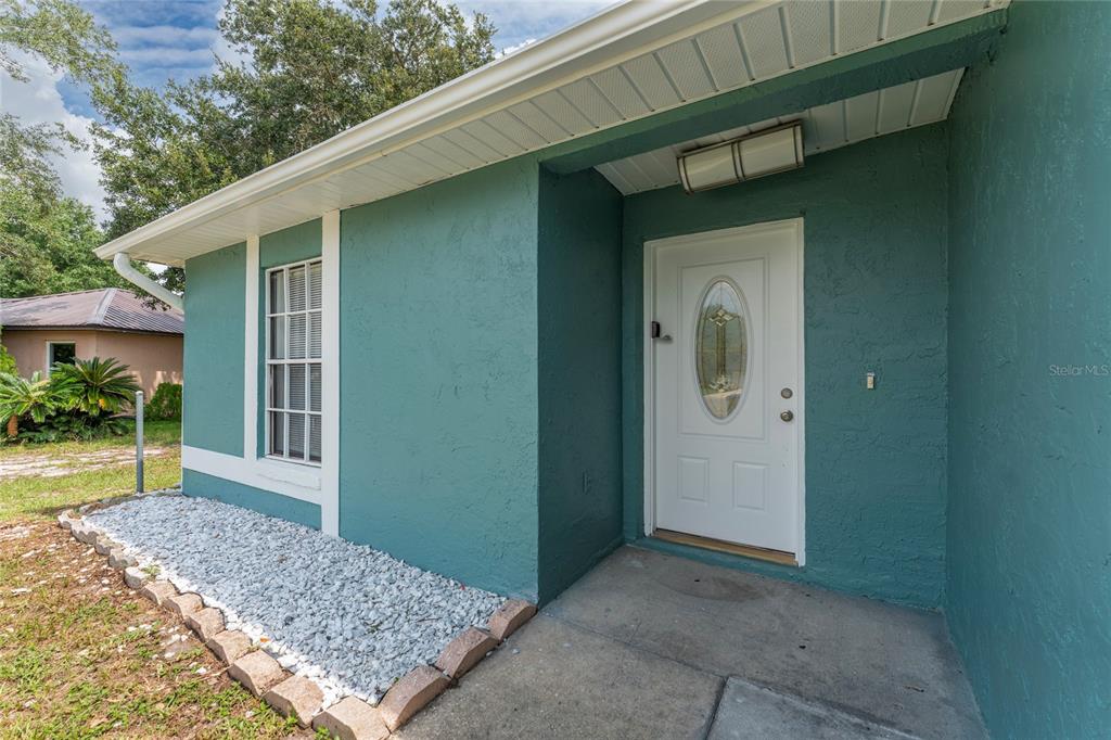 A teal-painted house exterior features a white front door with an oval glass insert — 913 SAN RAFAEL WAY, KISSIMMEE, FL