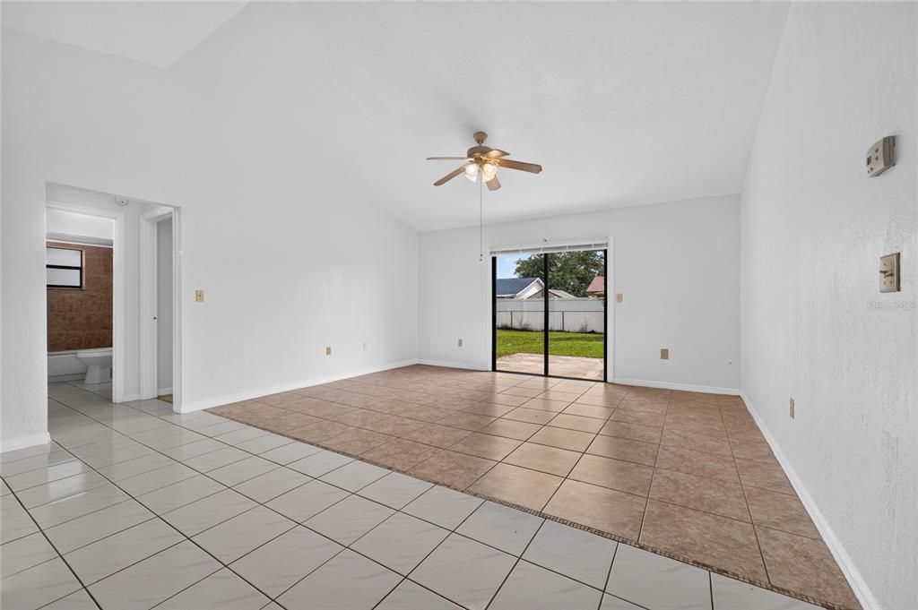 An empty living room features vaulted ceilings, a ceiling fan, and a mix of tile flooring — 913 SAN RAFAEL WAY, KISSIMMEE, FL