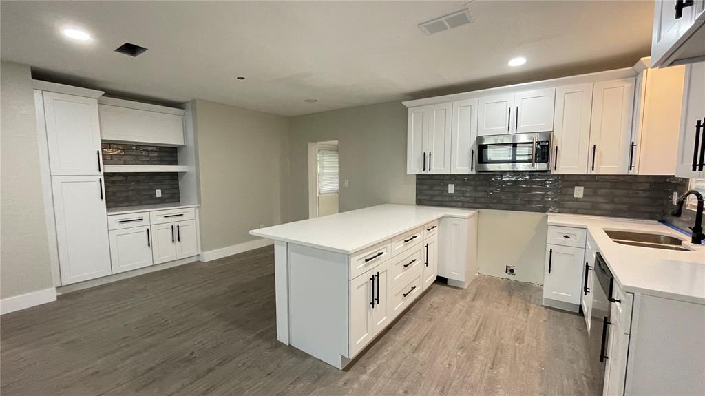 A kitchen features white cabinets, a central island, gray wood-look flooring, and a tiled backsplash — 2816 HARGILL DRIVE, ORLANDO, FL