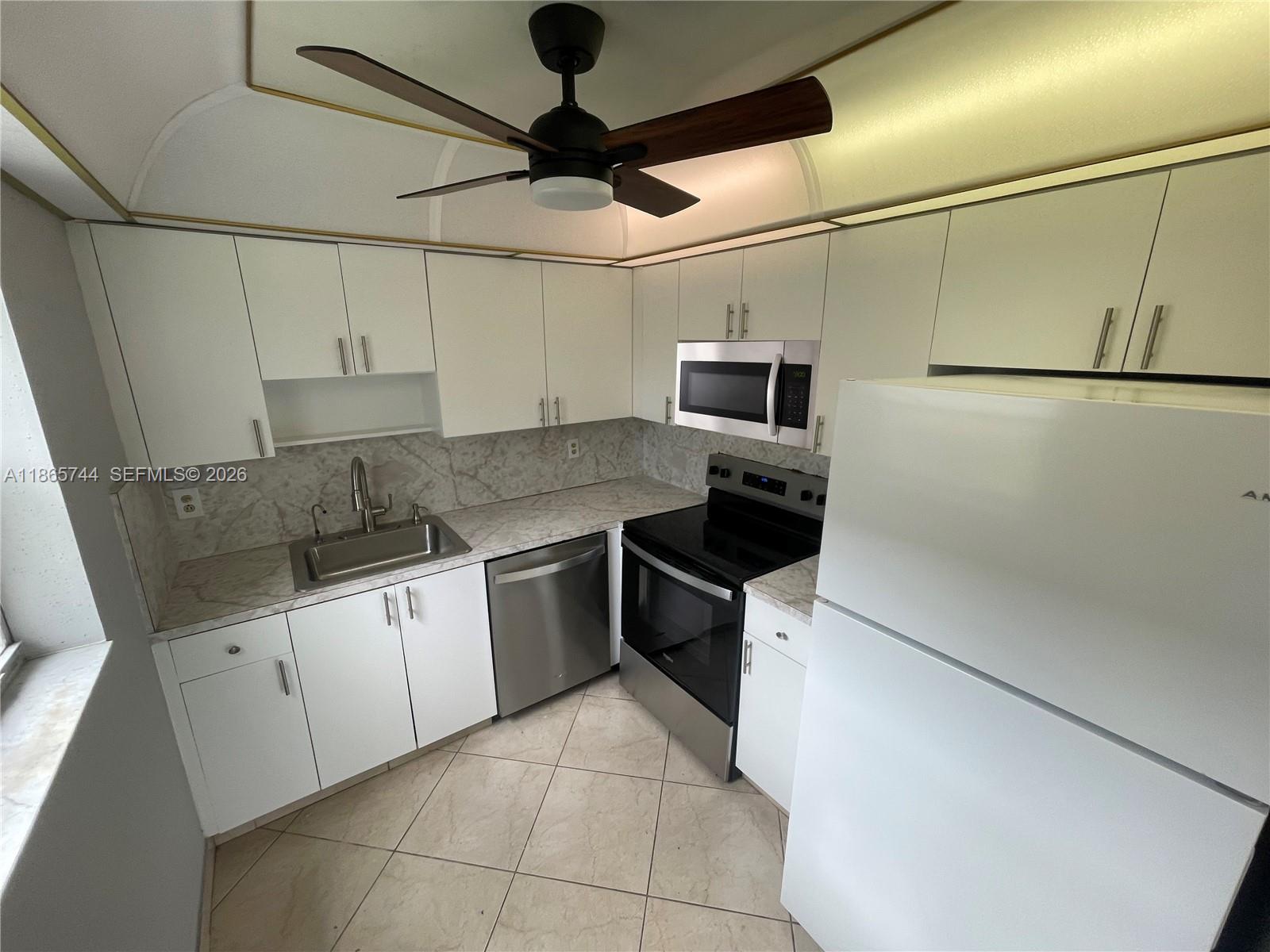 A kitchen features white cabinets, stainless steel appliances, marble-patterned countertops, and a ceiling fan — 101 Brittany # C, Delray Beach FL 33446, DELRAY BEACH, FL