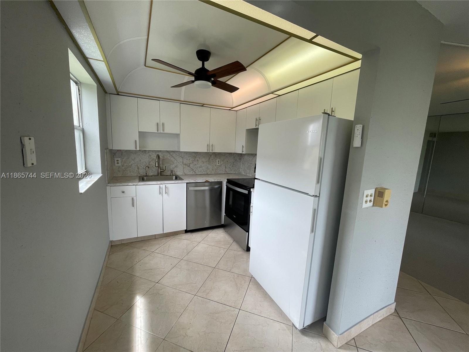 A kitchen features white cabinets, stainless steel appliances, a ceiling fan, and light-colored tile flooring — 101 Brittany # C, Delray Beach FL 33446, DELRAY BEACH, FL