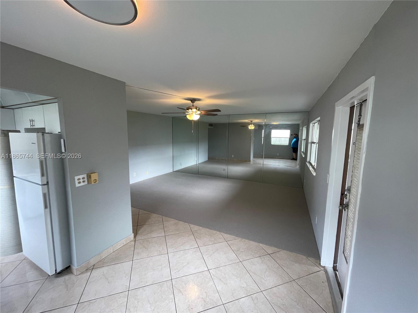 A living room features gray walls, carpeted flooring, a mirrored wall, and a ceiling fan — 101 Brittany # C, Delray Beach FL 33446, DELRAY BEACH, FL