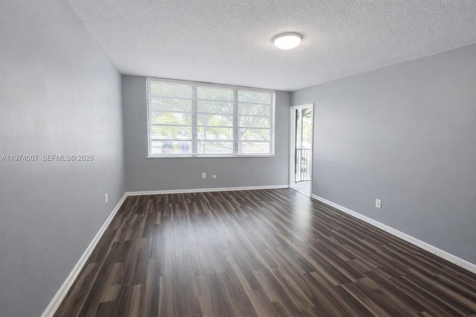 An empty room features gray walls, dark wood-look flooring, a large window, and a balcony door — 1780 NE 191st St # 2, Miami FL 33179, MIAMI, FL
