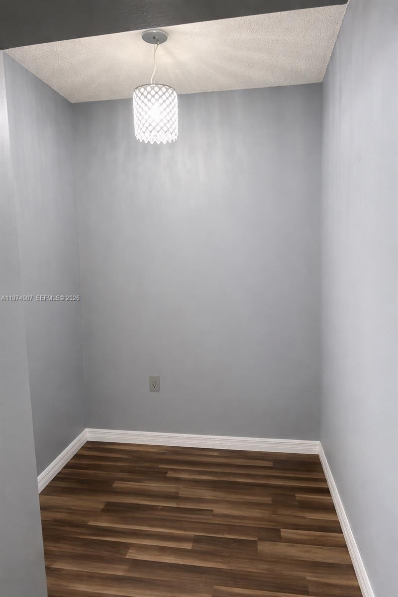 A small, empty room features gray walls, dark wood-look flooring, and a decorative pendant light — 1780 NE 191st St # 2, Miami FL 33179, MIAMI, FL