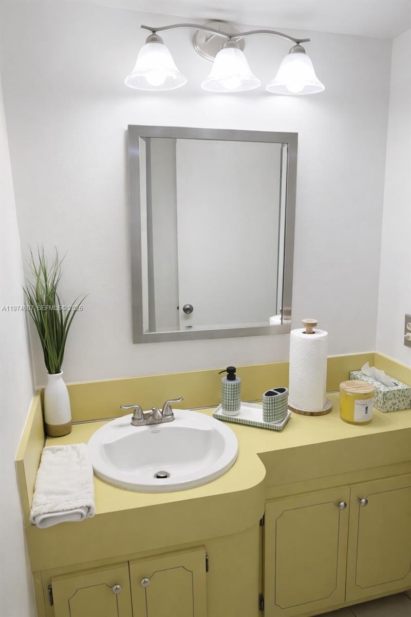 A bathroom features a yellow vanity, a white sink, and a rectangular mirror — 1780 NE 191st St # 2, Miami FL 33179, MIAMI, FL