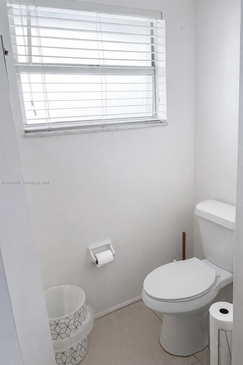 A small bathroom features a white toilet, a toilet paper holder, and a window with blinds — 1780 NE 191st St # 2, Miami FL 33179, MIAMI, FL