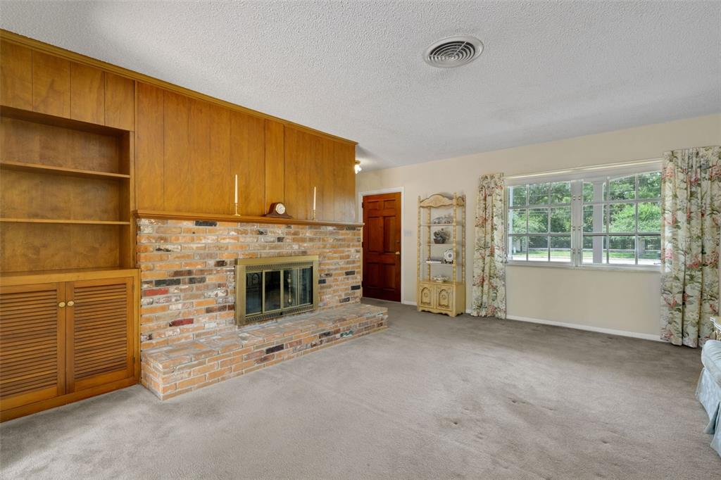 A living room features a brick fireplace, wood paneling, built-in shelving, and wall-to-wall carpeting — 4200 CLEVELAND HEIGHTS BOULEVARD, LAKELAND, FL