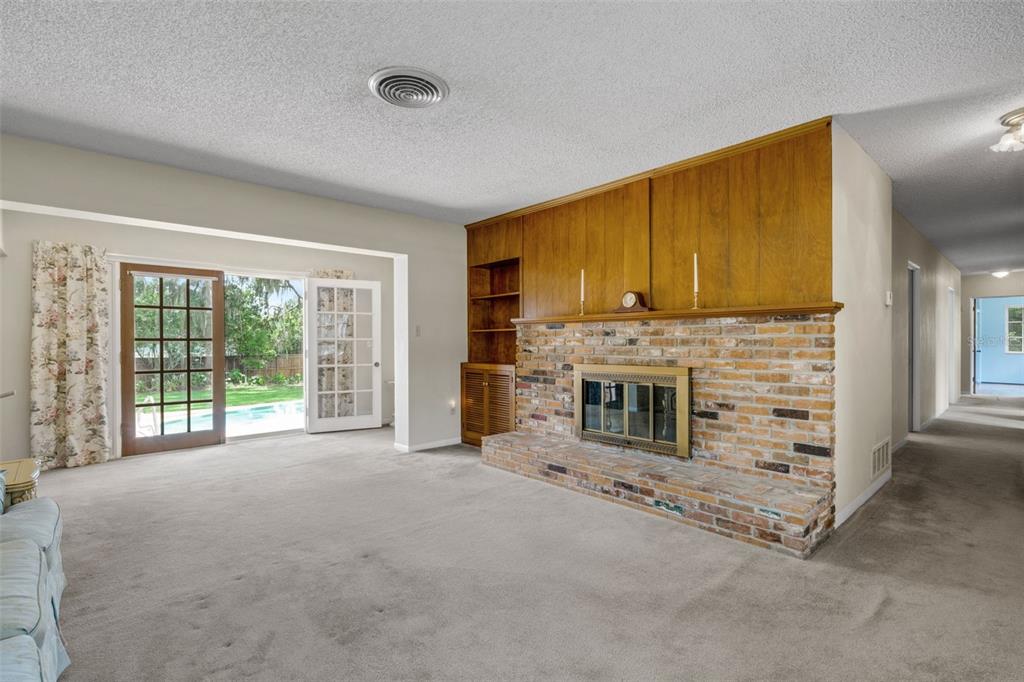 A living room features a brick fireplace, wood paneling, carpeted floors, and glass patio doors — 4200 CLEVELAND HEIGHTS BOULEVARD, LAKELAND, FL