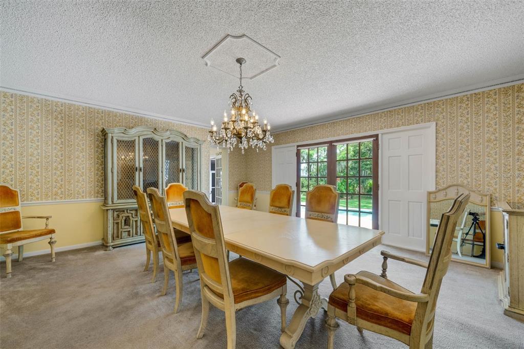 A dining room features a long table, upholstered chairs, a crystal chandelier, and patterned wallpaper — 4200 CLEVELAND HEIGHTS BOULEVARD, LAKELAND, FL