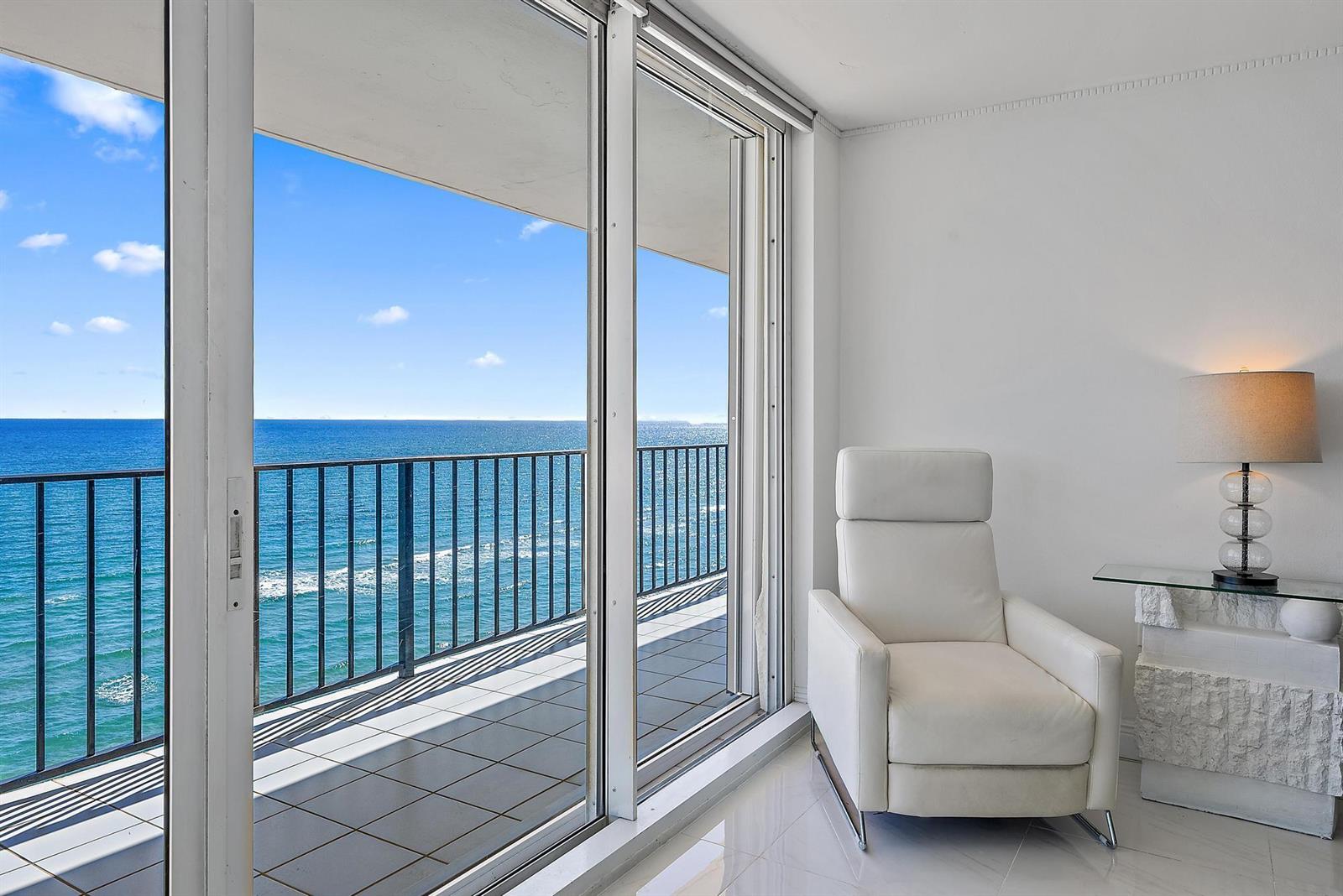 A white armchair sits next to a glass-topped table by a balcony overlooking the ocean — 3456 S Ocean Boulevard # 802, Palm Beach FL 33480, PALM BEACH, FL