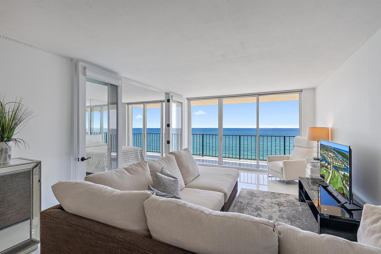 A living room with a beige sectional sofa, glass doors, and a view of the ocean — 3456 S Ocean Boulevard # 802, Palm Beach FL 33480, PALM BEACH, FL