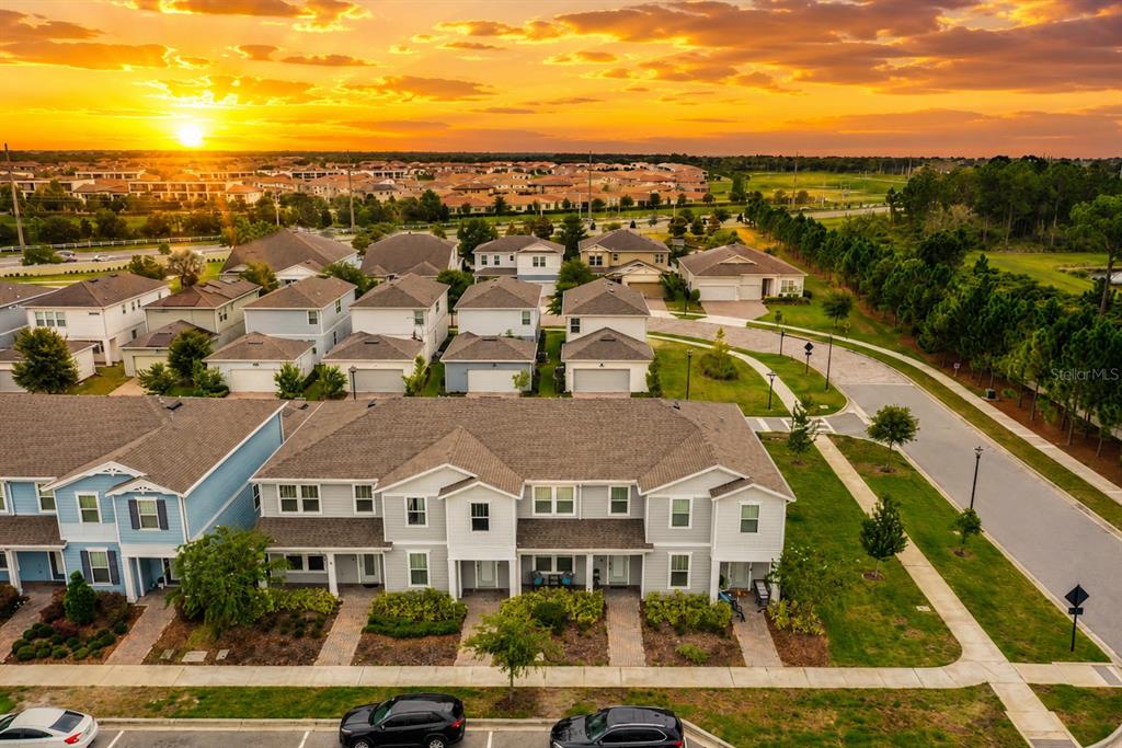 An aerial view shows a row of suburban townhouses at sunset with parked cars below — 14557 ORCHID ISLAND DRIVE, ORLANDO, FL