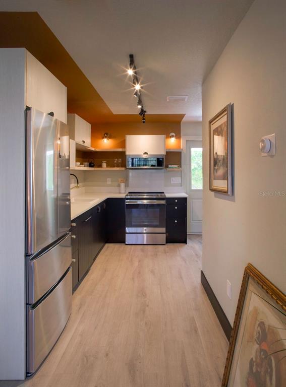A modern kitchen features dark lower cabinets, stainless steel appliances, and a warm orange ceiling — 6990 GREVILLA AVENUE S, SOUTH PASADENA, FL