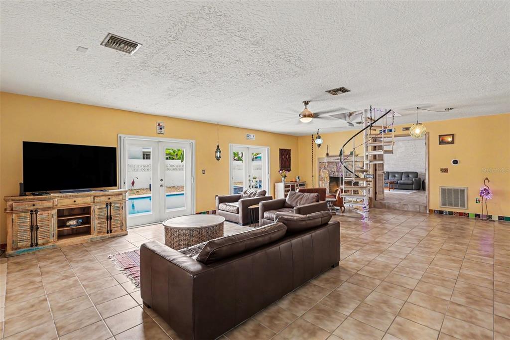 A living room with tile floors, a spiral staircase, and a large television console — 315 E CENTRAL BOULEVARD, CAPE CANAVERAL, FL