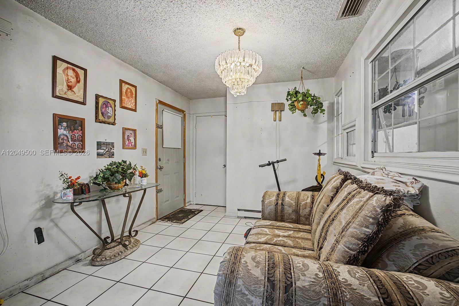 A living room features a patterned sofa, tile flooring, a crystal chandelier, and framed photos — 735 NW 8th Ct, Florida City FL 33034, FLORIDA CITY, FL