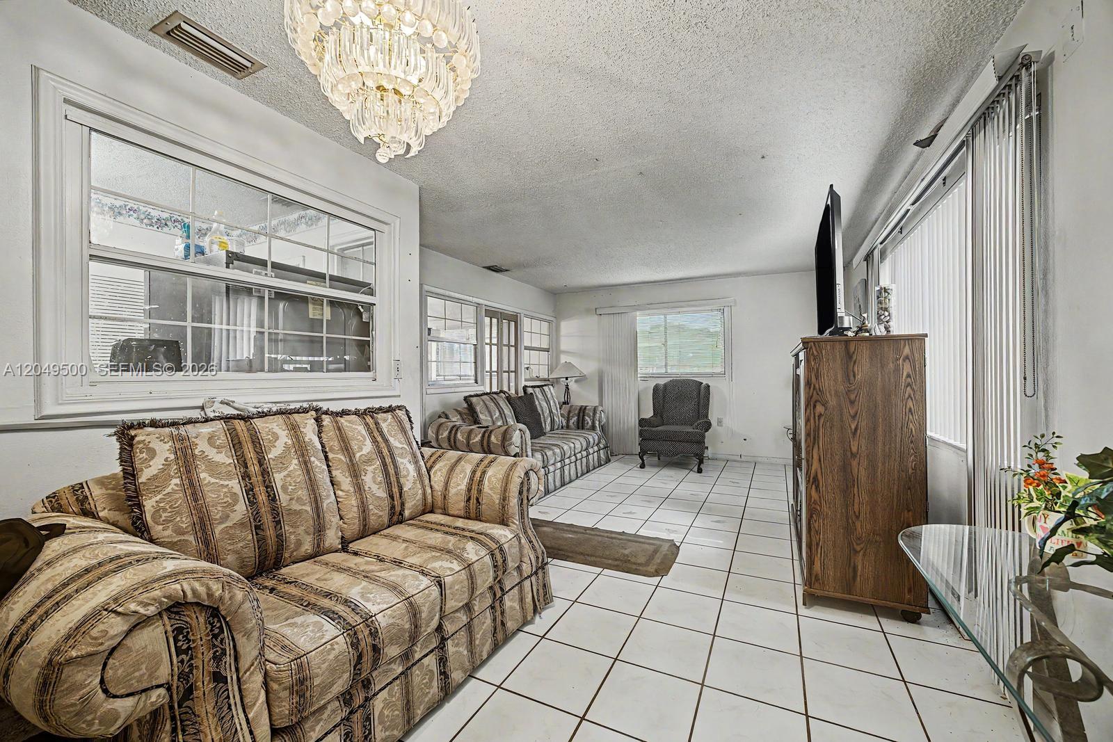 A living room features white tile flooring, a crystal chandelier, and two patterned sofas — 735 NW 8th Ct, Florida City FL 33034, FLORIDA CITY, FL