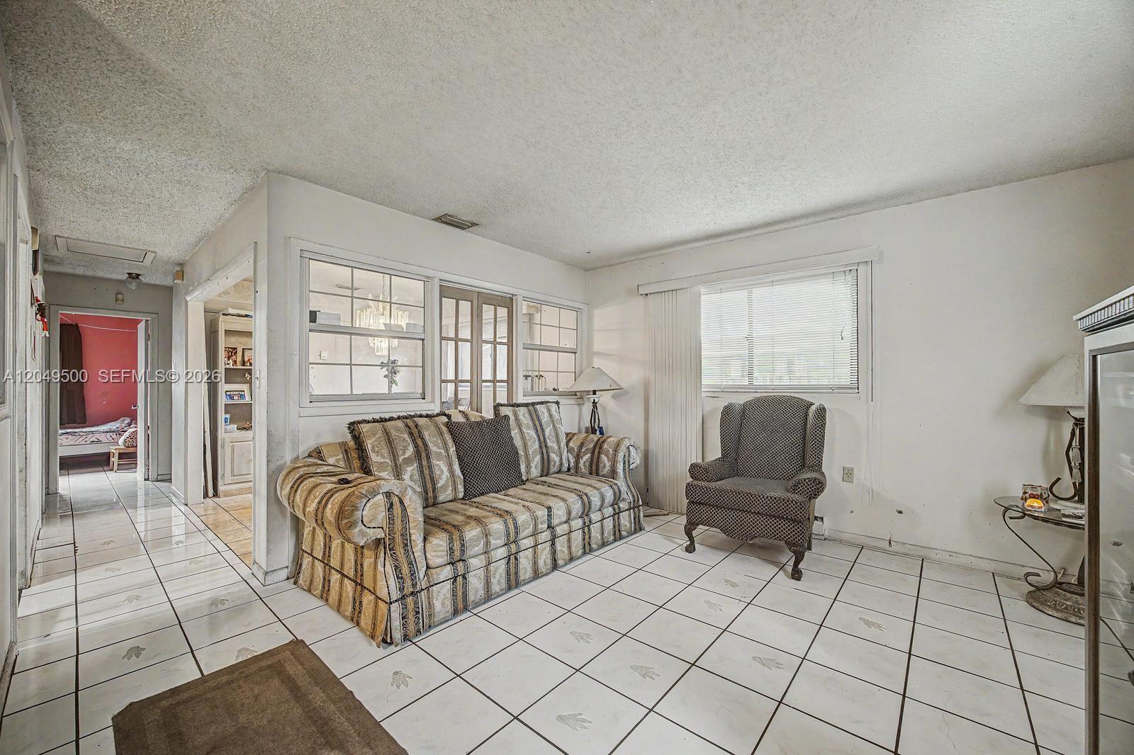 A living room features white tile floors, a patterned sofa, an armchair, and a window — 735 NW 8th Ct, Florida City FL 33034, FLORIDA CITY, FL