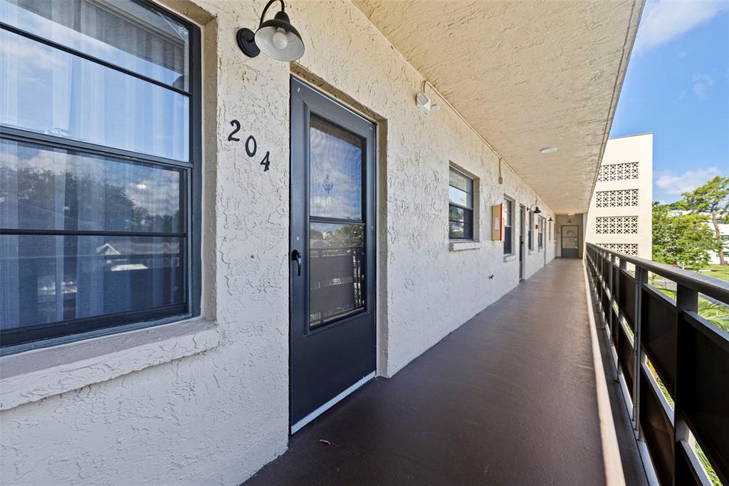 An exterior walkway leads to the entrance of apartment 204 in a multi-story building — 5975 TERRACE PARK DRIVE N UNIT 204, ST PETERSBURG, FL