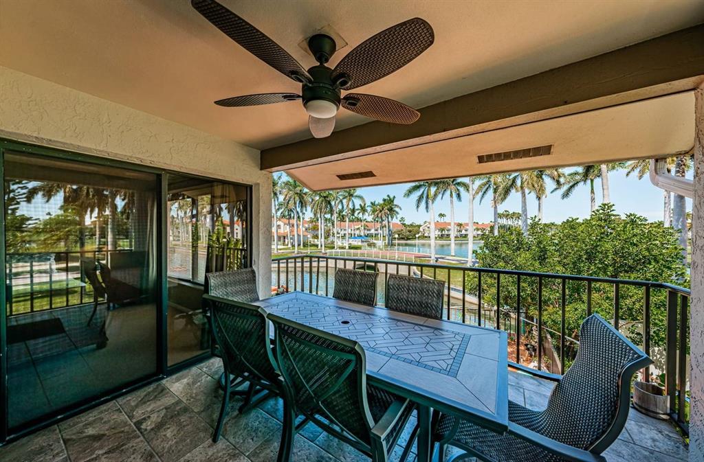 A covered balcony with a dining set, ceiling fan, and views of a lake and palms — 6273 BAHIA DEL MAR BOULEVARD UNIT 216, ST PETERSBURG, FL