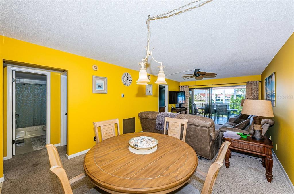A dining area with a round wooden table sits before a living room with yellow walls — 6273 BAHIA DEL MAR BOULEVARD UNIT 216, ST PETERSBURG, FL