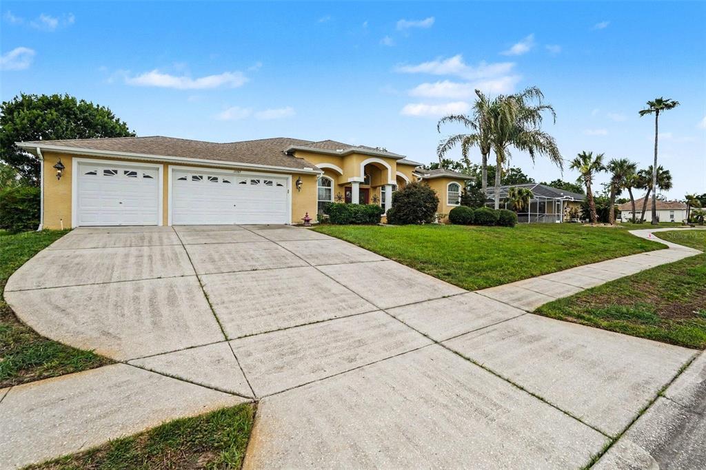 A yellow single-story house with a three-car garage and a concrete driveway — 13387 NEWCASTLE AVENUE, SPRING HILL, FL