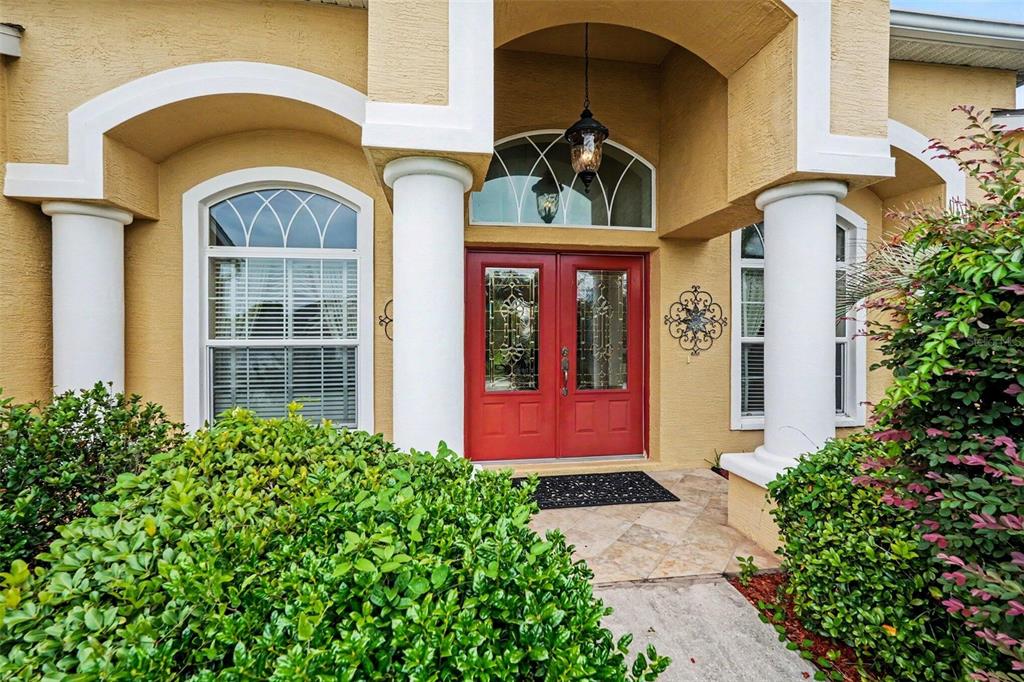 The front entrance features a red double door, white columns, and a tan stucco exterior — 13387 NEWCASTLE AVENUE, SPRING HILL, FL