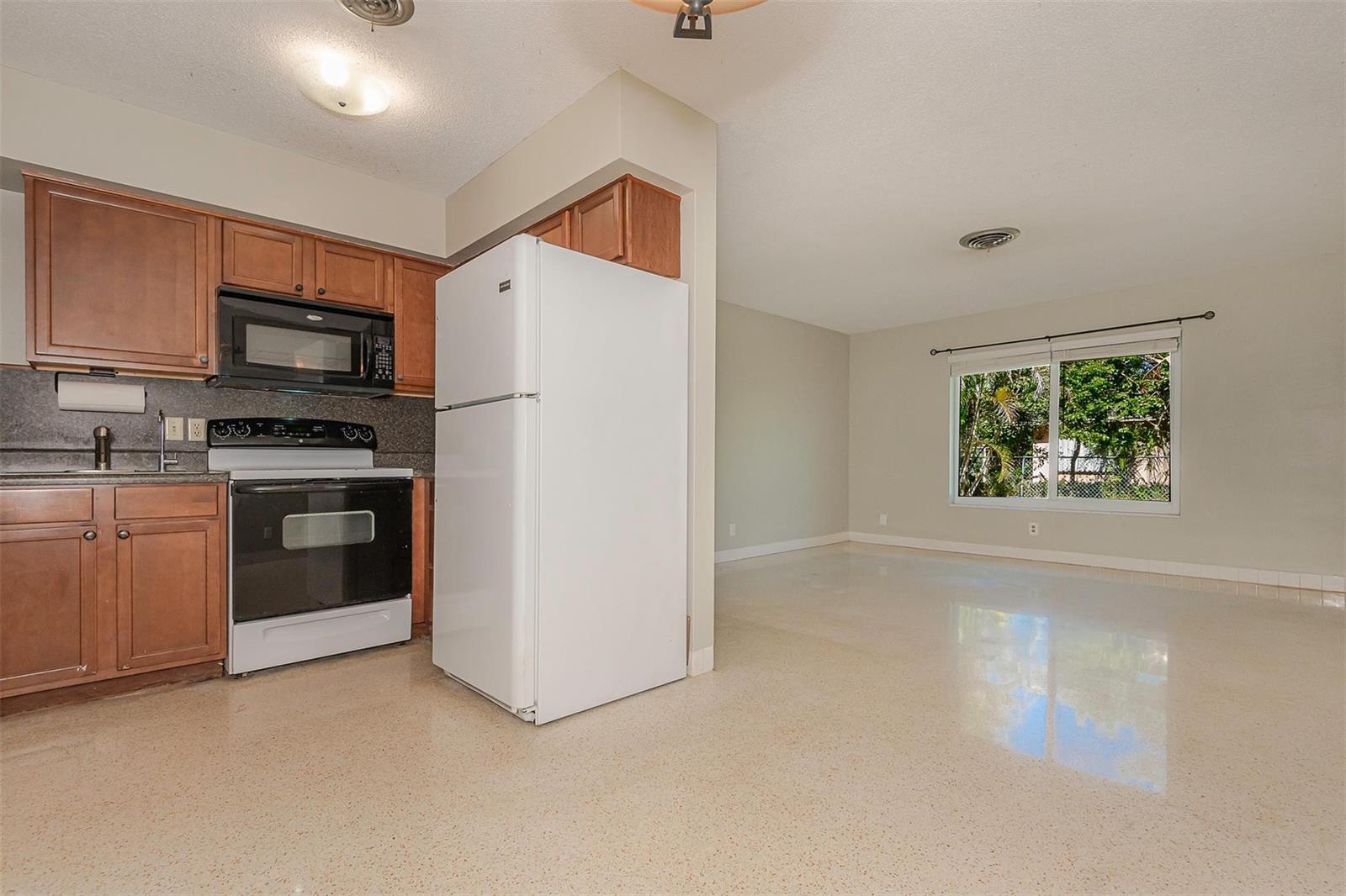 A kitchen with wood cabinets and white appliances opens into a spacious, light-filled living area — 321 SE 1st Avenue, Pompano Beach FL 33060, POMPANO BEACH, FL