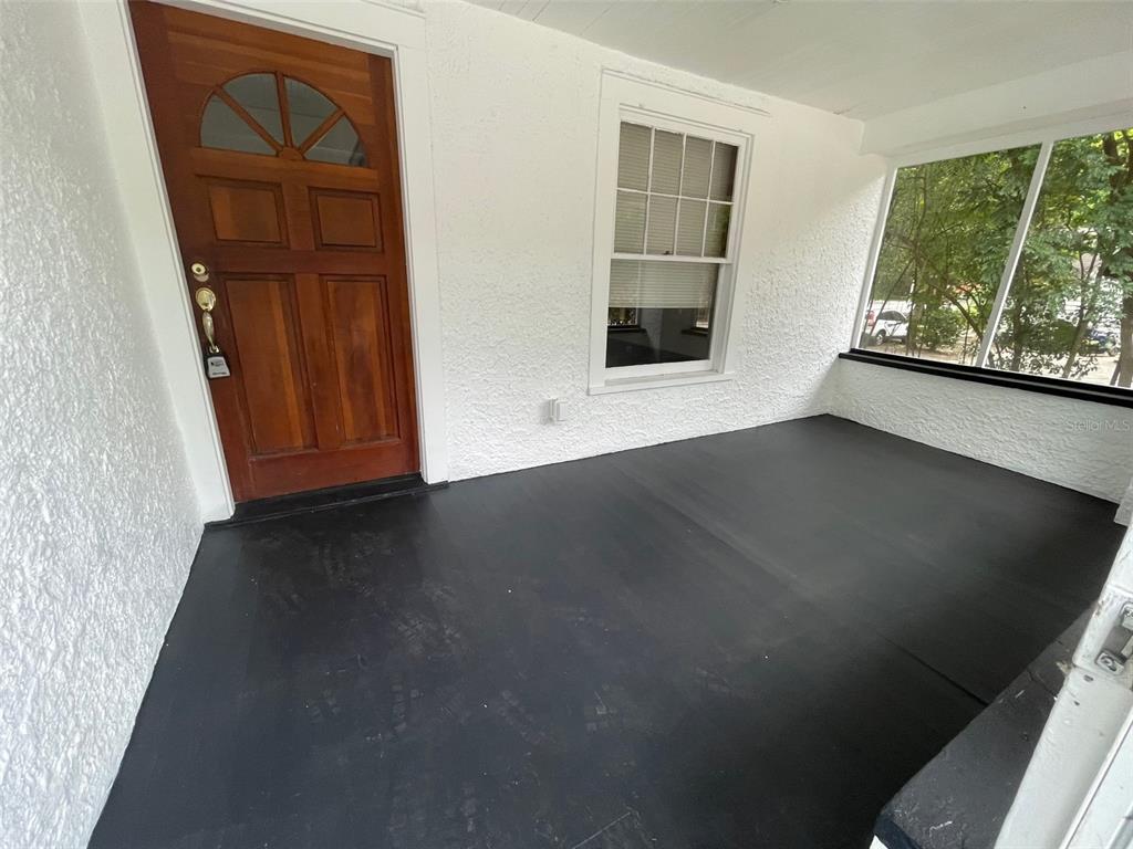 A covered porch features a wooden front door, white textured walls, and a black floor — 2635 W UNIVERSITY AVENUE, GAINESVILLE, FL