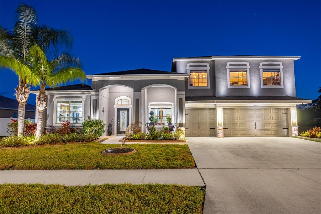 A two-story suburban house with a three-car garage and a palm tree at dusk — 2504 CUMBERLAND CLIFF DRIVE, RUSKIN, FL