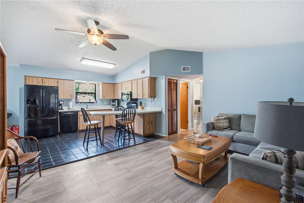 An open-concept living room and kitchen with light blue walls and wood-look tile flooring — 12510 PAYSON STREET, NEW PORT RICHEY, FL