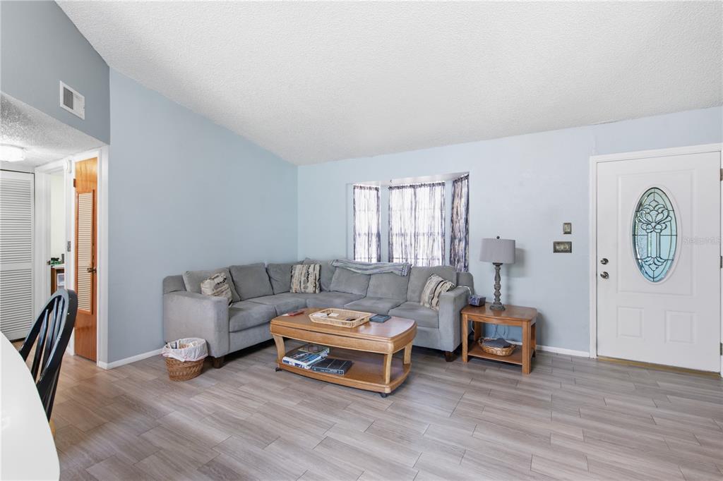 A living room features light blue walls, gray wood-look flooring, a sectional sofa, and a door — 12510 PAYSON STREET, NEW PORT RICHEY, FL