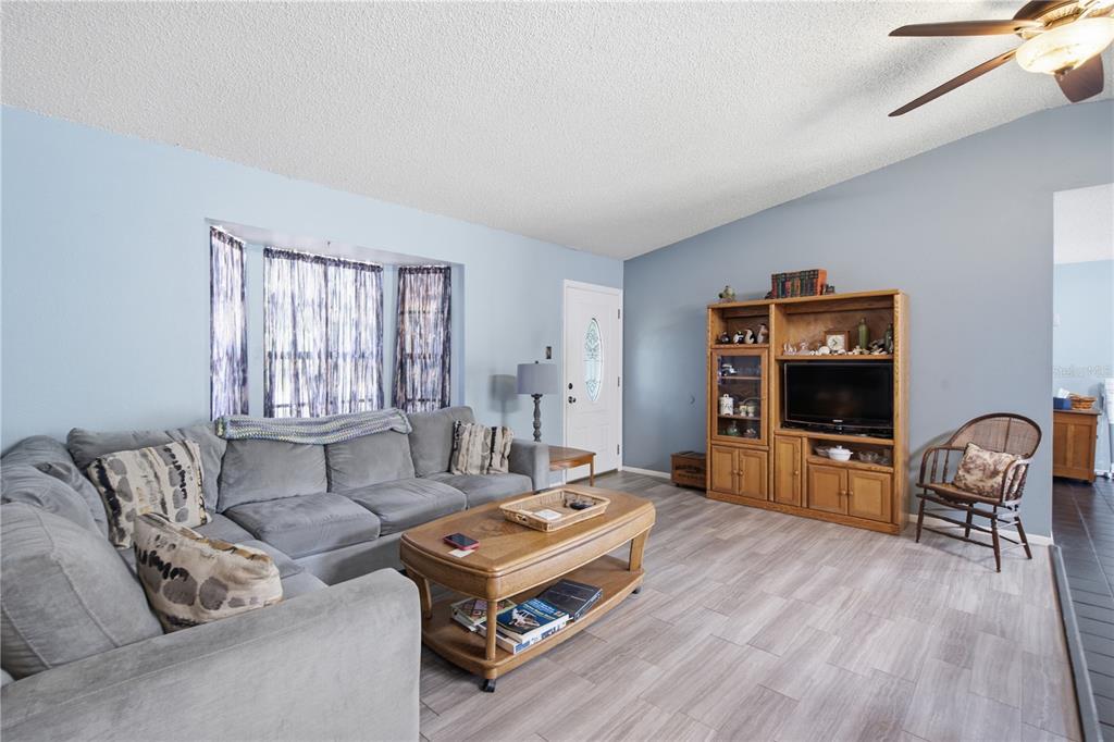 A living room features a grey sectional sofa, wooden coffee table, entertainment center, and ceiling fan — 12510 PAYSON STREET, NEW PORT RICHEY, FL