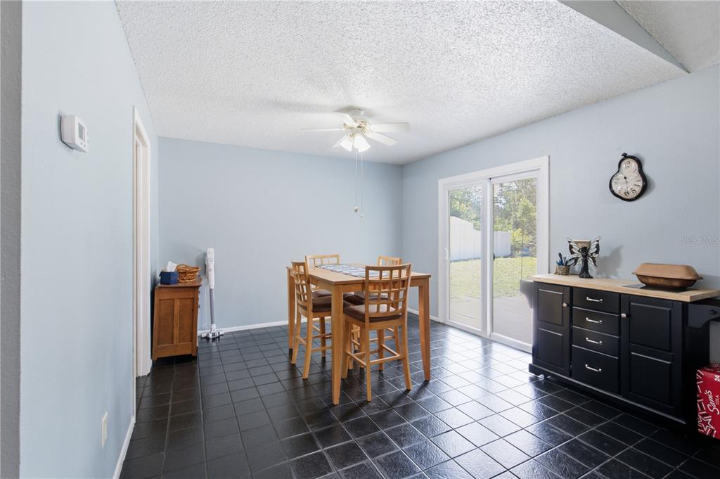 A dining room with light blue walls, black tile flooring, a wooden table, and sliding doors — 12510 PAYSON STREET, NEW PORT RICHEY, FL