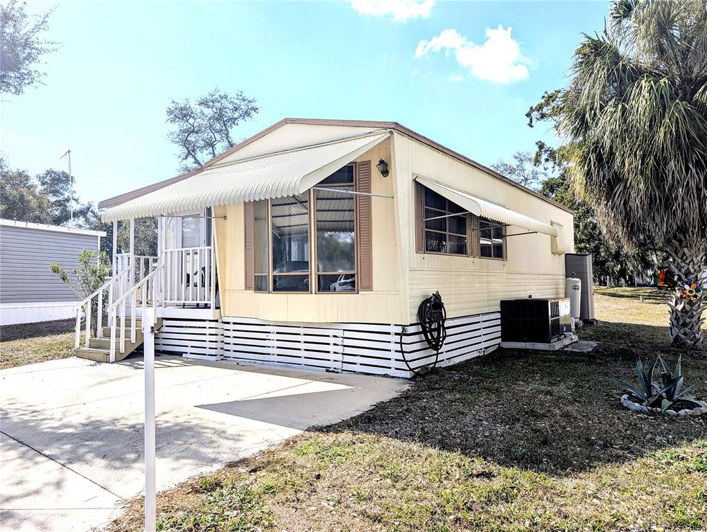 A light yellow mobile home with a white porch, metal awnings, and a concrete driveway — 3300 26TH AVENUE E UNIT 31, BRADENTON, FL