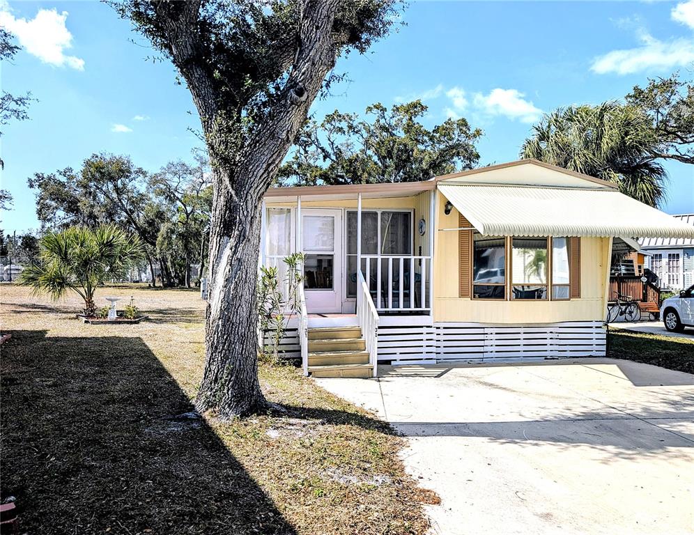 A yellow mobile home features a front porch, white lattice skirting, and a concrete driveway — 3300 26TH AVENUE E UNIT 31, BRADENTON, FL